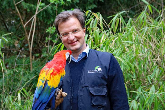 Директор зоопарка Маттиас Райншмидт с красным арой у входа в новый вольер